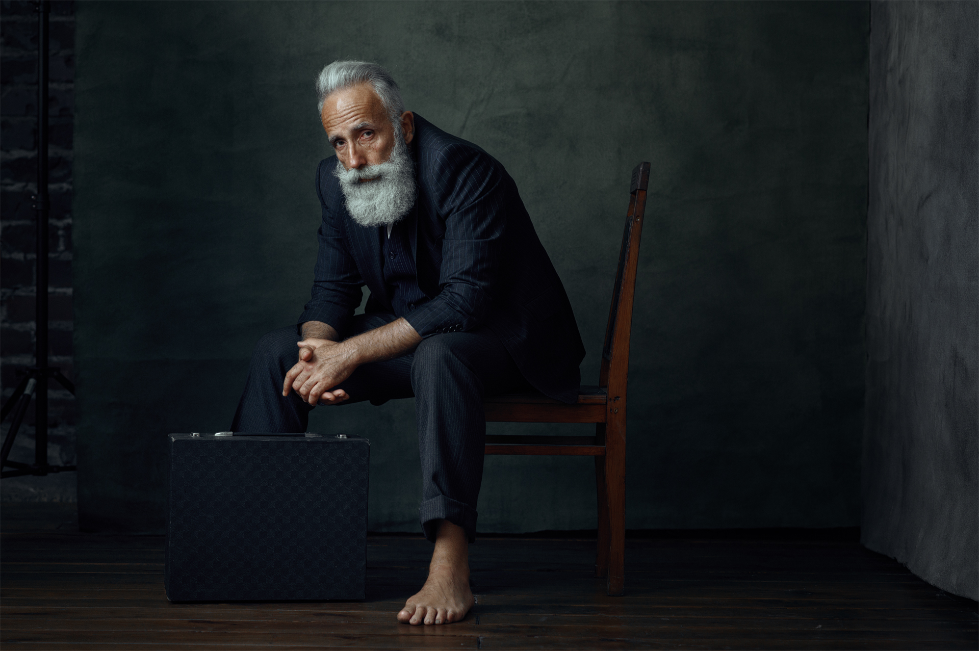 Studio portrait of a bearded man in a pinstripe suit, seated against a dark wall — magazine work by Hamudi Leon