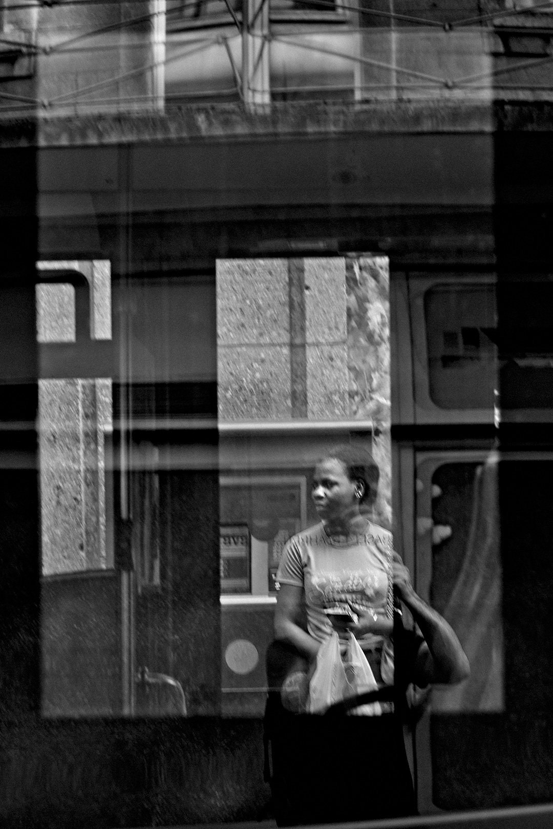 Woman with shopping bags seen through the layered reflections of a shop window — street photograph by Hamudi Leon