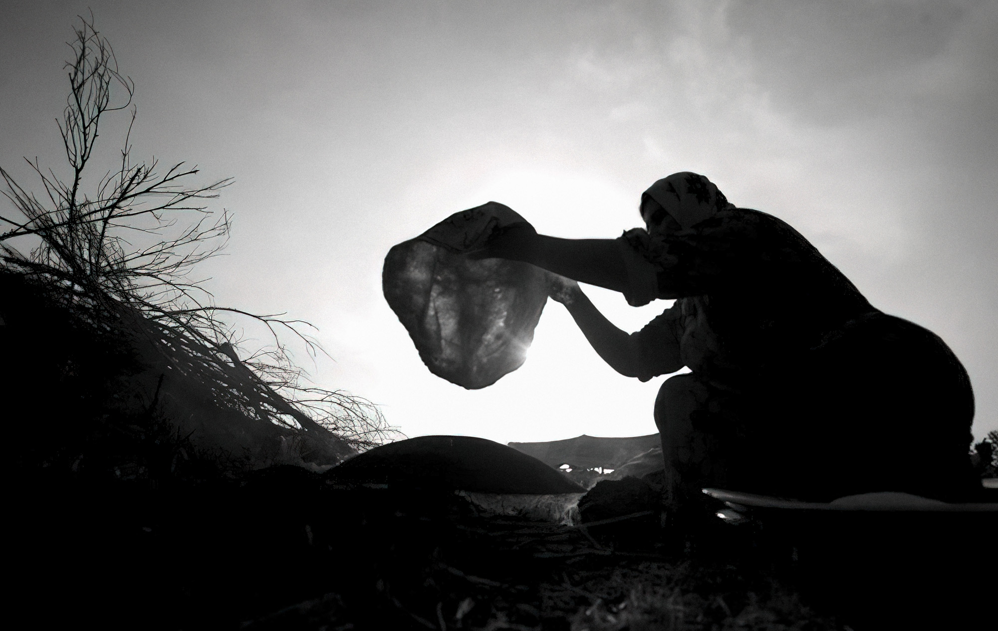 Backlit silhouette of a woman shaking out a cloth against a bright sky — street photograph by Hamudi Leon